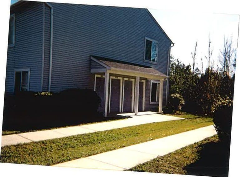 A blue-gray Lexington Village building with a covered porch entry and a paved walkway leading up to the door