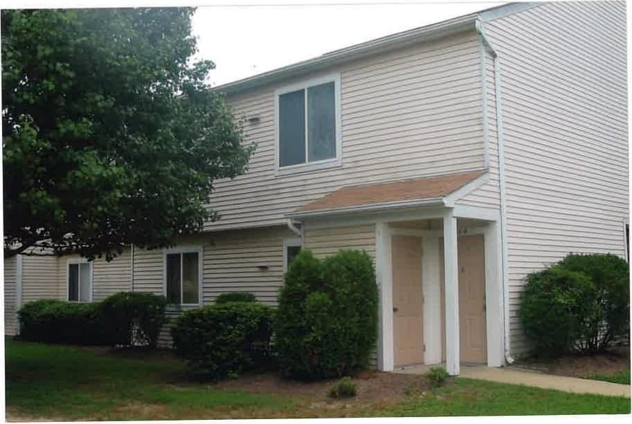 A two-story Lexington Village building with cream siding, two front doors, and a shade tree on the lawn