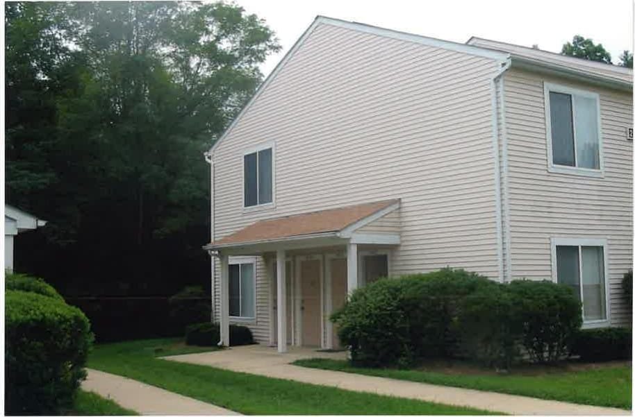 A cream-sided Lexington Village building with a covered porch entry, framed by trimmed shrubs and trees